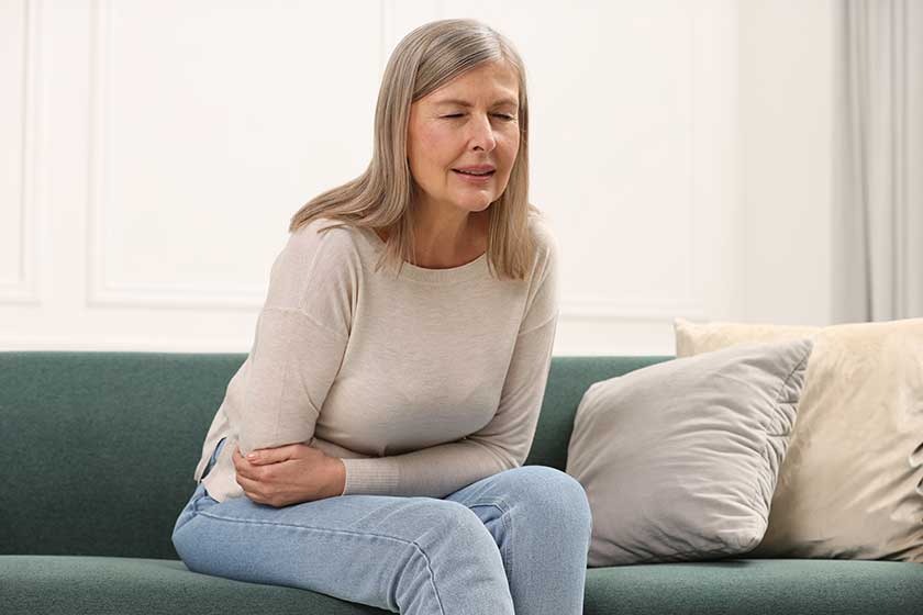 Menopause. Woman suffering from abdominal pain on sofa at home