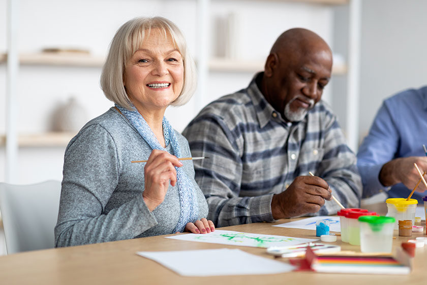 Positive senior woman enjoying painting with brush